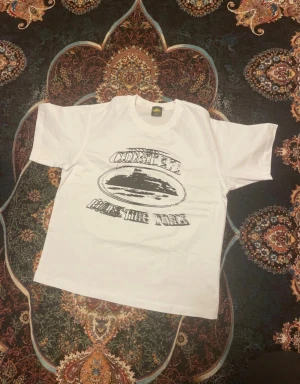 Vit t-shirt med tryck från Tank - Säljer en vit t-shirt i 100% bomull från Tank, storlek small. T-shirten har ett svart grafiskt tryck på framsidan med text och motiv. Klassisk rund hals och korta ärmar. Perfekt för dig som gillar streetwear och vill ha en enkel men cool look.