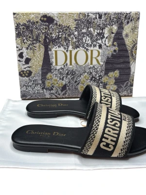 Di🅾️r tofflor  - Snygga sandaler  med broderad logga på remmen i svart och beige. Platt sula i skinn och öppen tå. Lyxig design med klassiska färger och detaljer, perfekt för dig som vill sticka ut med stil. 