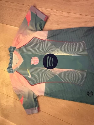 FC Barcelona fotbolls T-shirt Lamine Yamal - Säljer en FC Barcelona fotbolls T-shirt med Lamine Yamal och nummer 10 på ryggen. Västen har coola färgskiftningar i blått och rosa med vita linjemönster och tryckta loggor. Materialet är lätt polyester, perfekt för fotbollsträning eller bara chilla i hemmet