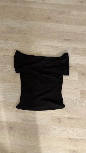 Svart offshoulder topp från H&M - Säljer en svart offshoulder topp från H&M i storlek XS. Toppen har en stilren och enkel design med axelbandslös passform och är tillverkad i mjukt syntetmaterial. Knappast använd och i nästan nytt skick. 