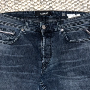 Replay Grover  - Snygga Replay Grover jeans i mörkblå tvätt med klassisk femficksdesign och raka ben. Jeansen har diskreta slitningar och silverfärgade detaljer vid fickorna. jeans med skön passform. Perfekt för dig som gillar stilrena och tidlösa jeans.