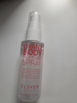 I Want Body Texture Spray Eleven - En genomskinlig sprayflaska med texten 'I Want Body Texture Spray' från Eleven Australia. Flaskan rymmer 50 ml och har en vit pump. Produkten är en lätt texturspray som kombinerar pulver och vätska för att ge håret volym och struktur. 