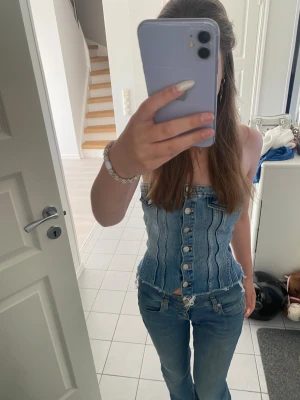 Denim tubtopp från Zara XS - Säljer en blå tubtopp i denim från Zara, storlek XS. Toppen har snygga silverfärgade knappar framtill, två fejkade fickor upptill och rå, fransig kant nedtill. Modellen är tight och axelbandslös, perfekt för dig som gillar party toppar 😋🥰