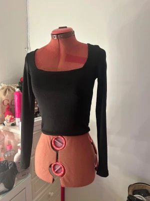 Svart långärmad topp med fyrkantig hals - Säljer en svart långärmad topp med snygg fyrkantig halsringning. Modellen är slim och croppad, vilket ger en modern och stilren look. Materialet är mjukt och stretchigt tyg!