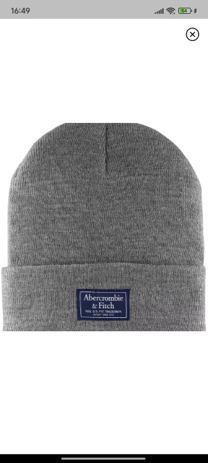  Abercrombie & Fitch Beanie - Snygg grå mössa från Abercrombie & Fitch med klassisk uppvikt kant och blå logotyp-patch framtill. Enkel och stilren design som passar perfekt till streetwear. Mjuk och skön stickad kvalitet som håller dig varm under kyliga dagar.