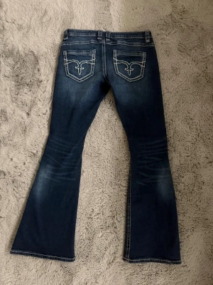Blå low rise flare jeans från Gina Tricot - Snygga mörkblå jeans med låg midja och flare-ben från Gina Tricot. Jeansen har slitna detaljer och hål på framsidan, klassisk femficksdesign och dekorativa sömmar på bakfickorna. Byxorna är i storlek M men skulle säga att det passar någon med storlek S. Aldrig använda bara testade!! 