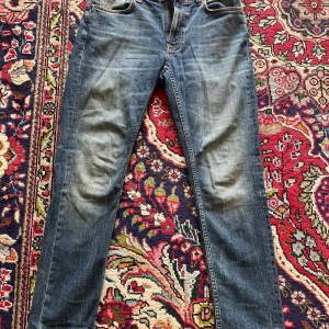 Blå jeans från Nudie, W31 L30 - Säljer ett par klassiska blå jeans från Nudie Jeans, modellen är lean dean.. den har fem fickor och Nudie-loggan på bakfickan. Jeansen är i bomull och har en normal passform. 