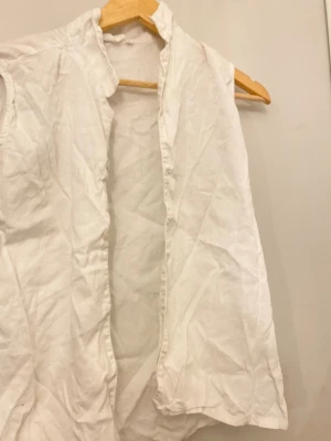 Vit ärmlös väst i bomull - Säljer en enkel vit väst i mjukt bomullstyg. Västen är ärmlös och har en rak, öppen design utan knappar eller dragkedja. Perfekt för att lägga till en clean och fräsch touch till din outfit.