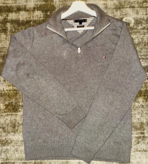 Tommy Hilfiger half zip  - Stilren och bekväm halfzip-tröja från Tommy Hilfiger i klassisk grå färg. Diskret Hilfiger-logga och hög krage med dragkedja. Materialet är mjukt, och tröjan är i bra skick