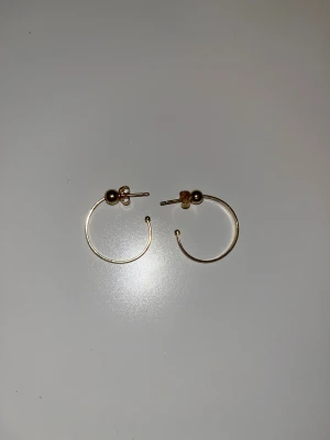 18K guldörhängen cirkel 21mm - Snygga örhängen i 18 karat guld med rund cirkelform, ca 21 mm i diameter och bredd mellan 1,5-4,5 mm. De har en minimalistisk design med en liten kula vid fästet och är perfekta för dig som gillar stilrena smycken.