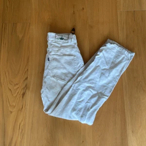 Vita Cannabis Jeans i rak modell - Snygga vita jeans från Cannabis Jeans med klassisk rak passform och coolt logopatch med grön cannabisblad på bakfickan. Jeansen har fem fickor, knapp med logga och är tillverkade i slitstarkt bomullsmaterial. Perfekt för dig som vill sticka ut med en unik detalj.