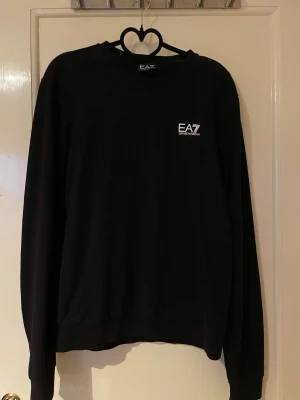 Svart långärmad tröja EA7 - Svart långärmad tröja från EA7 Emporio Armani med vit logga på bröstet. Mycket bra skick och säljs i befintlig skick. 