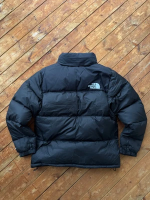The North Face 1996 Retro Nuptse - Svart The North Face 1996 Retro Nuptse dunjacka i storlek M. Klassisk, varm och stilren vinterjacka med ikonisk boxig passform. Jackan är helt ny med prislapp kvar – perfekt för kalla vinterdagar