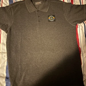 Pike ifrån sofialäktaren 2018 - Snygg grå pikétröja från Mac One i storlek S med Djurgården Stockholm-märke på bröstet. Klassisk krage, tre knappar och korta ärmar. Perfekt för dig som vill visa ditt lagstöd med stil.