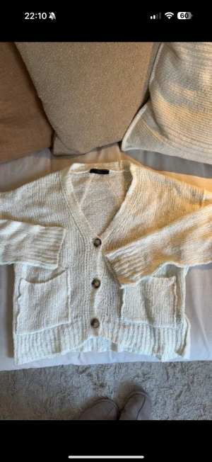 Beige stickad kofta med knappar - Mysig beige stickad kofta från Gina Tricot med v-ringning och tre stora knappar framtill. Koftan har två praktiska fickor och ribbade muddar vid ärmslut och nederkant. Perfekt för lager-på-lager och chill dagar.