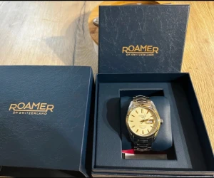 Roamer herrklocka med guldfärgad urtavla - Snygg herrklocka från Roamer med guldfärgad urtavla och silverfärgat armband i metall. Klockan har datumvisning och klassisk rund form. Perfekt accessoar för dig som gillar stilrena detaljer och schweizisk design.