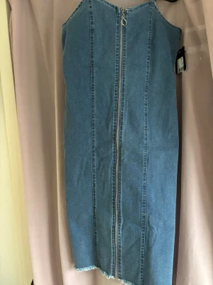 Blå jeansklänning med dragkedja - Snygg blå jeansklänning från Y.A.S med smala axelband och hel dragkedja framtill. Klänningen har en rak passform och rå kant nedtill för en cool touch. Perfekt för dig som gillar denim och vill ha en enkel men trendig look.