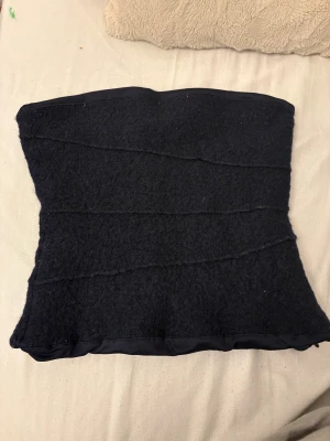 Elegant svart bandeau tubtopp från Zara - Säljer en svart bandeau tubtopp från Zara i storlek XS. Toppen har en mjuk, stickad känsla med subtila vågiga sömmar och satinkant upptill och nedtill. Perfekt för dig som gillar minimalistisk och stilren design. 