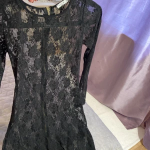 Svart spetsklänning från Vila XS - Supersnygg svart kortklänning från Vila i storlek XS. Klänningen är helfodrad med transparent spets och har ett blommigt mönster. Långärmad modell med rund hals och dragkedja i ryggen som ger en cool detalj. Perfekt för dig som gillar stilrena och trendiga plagg.kan även passa S,36 eftersom den är lite stretch. Mycket elegant för fest man kan ha lång linne under den färg man gillar, röd för jul osv.