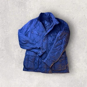 Barbour Quilted jacka - Snygg och klassisk Barbour International quiltad jacka i svart. Lätt och bekväm modell med tryckknappar, fyrficka-design och Barbour-logga på ärmen. Perfekt till höst/vår och funkar både till streetwear och mer clean stil.  Skick: ✔ Bra begagnat skick ✔ Inga hål eller fläckar ✔ Quiltningen och sömmarna är fina ✔ Endast normalt bruksslitage  Detaljer: • Färg: Svart • Modell: Field / International Quilt • Lättvikt, bekväm passform • Dragkedja + tryckknappar  Perfekt jacka för dig som vill ha Barbo