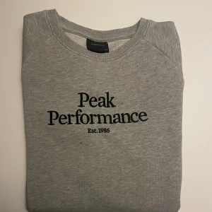 Grå Peak Performance tröja - Det är en grå tröja med broderad logga. Den är väldigt skön att ha på och jag har använt den inte så ofta.