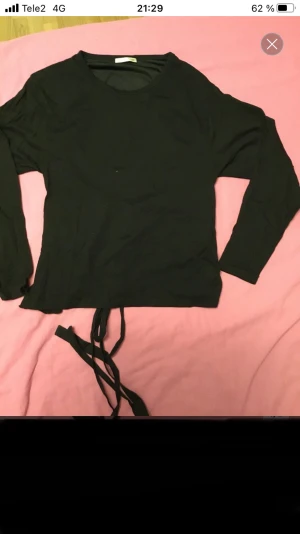 Svart långärmad topp med öppen rygg och knyt - Svart långärmad topp med rund hals och snygga knytband i midjan. Baksidan har en öppen rygg med band som kan knytas för en cool detalj. Materialet känns mjukt och lätt, perfekt för dig som gillar stilrena plagg med twist.