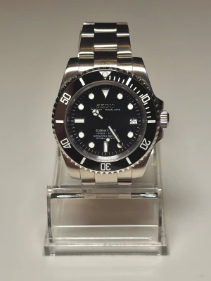 Seiko mod Black Submariner 40mm - Helt oanvänd Seiko Submariner mod med svart boett. Utrustad med Seikos NH35 urverk, med hållbart safirglas och en gridlock clasp, samma typ som används på en del rolexklockor som gör det lätt att justera klockans längd. DM mig om du vill ha fler bilder eller undrar något. Extra länkar följer också med. Pris är diskuterbart.