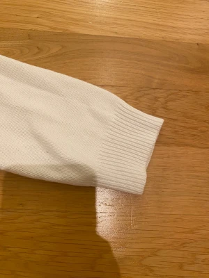 Vit stickad tröja med Union Jack från Solid - Vit stickad tröja från Solid i storlek M med långärmad passform och ribbade muddar. På bröstet finns ett stort Union Jack-tryck i marinblått och vinrött. Rund halsringning och mjukt material.