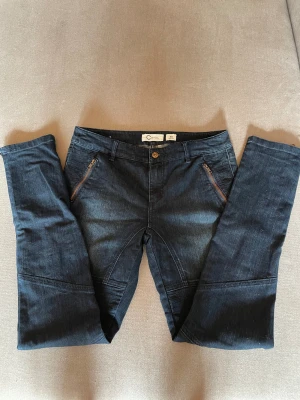 Mörkblå jeansbyxor med dragkedjor - Snygga mörkblå jeansbyxor från Cubus med coola dragkedjor vid fickorna och bensluten. Byxorna har raka ben, normal passform och är tillverkade i jeansmaterial. Perfekt för dig som gillar detaljer och en stilren look.