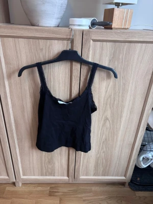 Svart topp med spets  - Säljer en svart linnetopp från  lager 157  i storlek M. Toppen har tunna axelband och är dekorerad med spets längs kanterna. 