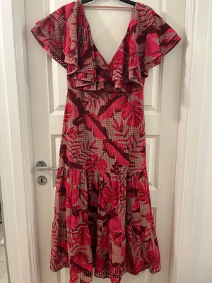 Blommig långklänning Johanna Ortiz x H&M - Säljer en superfin långklänning från Johanna Ortiz x H&M i beige och rött med blommigt mönster. Klänningen har v-ringning, volangdetaljer vid axlarna och knappar framtill. Tillverkad i bomull med luftig känsla och korta ärmar.