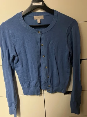Blå kofta från H&M XS - Blå kofta från H&M i storlek XS. Modellen har rund hals, långa ärmar och knappar framtill. Materialet är mjukt och består av 72% viskos och 28% polyamid. Perfekt att slänga på sig när det är lite kyligt ute.