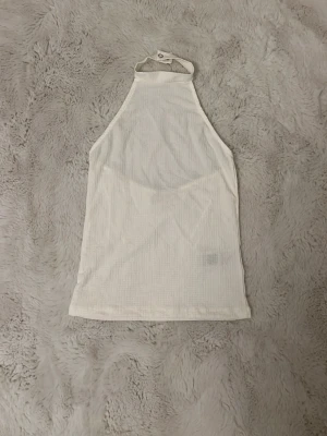 Vit halterneck linnetopp från Nelly - Säljer en vit halterneck linnetopp från Nelly i storlek XS. Toppen har en hög hals med knappstängning i nacken, öppen rygg och är ärmlös. Materialet är strukturerat och lätt, perfekt för varma dagar. Enkel och stilren design som passar till mycket. Oanvänd 