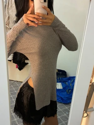 Grå ribbad långärmad topp med slits - Säljer en grå ribbad långärmad topp med höga slitsar på sidorna. Toppen har en tight passform och är tillverkad i ett mjukt stickat material. 