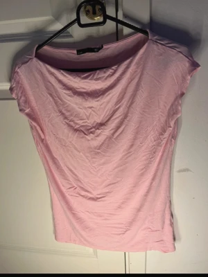 Ljusrosa tröja med korta ärmar - Säljer en ljusrosa tröja från lager 157 med korta ärmar och rundad hals. Toppen är gjord i mjuk bomull och har en enkel, feminin design som är lätt att matcha med olika outfits. Perfekt för vår och sommar!