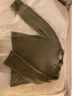 Olivgrön stickad tröja från H&M - Säljer en olivgrön stickad tröja från H&M i storlek 158/164. Tröjan har en rund hals med ribbad kant och långa ärmar med breda muddar. Materialet är mjukt och har en grovstickad struktur som ger en chill och avslappnad vibe.