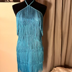 Blå fransklänning med halterneck - Supersnygg blå kortklänning med halterneck och massor av fransar som ger en riktigt cool look. Klänningen knyts i nacken och har en figurnära passform. Perfekt för dig som vill sticka ut och älskar att dansa!