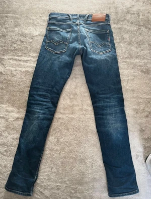 Replay Anbass slim fit jeans blå - Säljer ett par Replay Anbass jeans i slim fit, storlek w29 L32. De är mörkblå med snygga slitningar och klassiska fem fickor. Jeansen har kontrastsömmar och en läderpatch bak i midjan. Perfekt passform för dig som gillar smalare jeans.