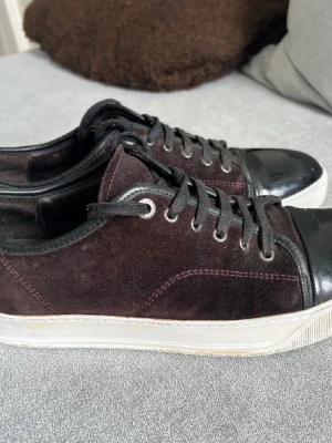 Snygga Lanvins - Snygga Lanvins i mörkbrun mocka med svarta läderdetaljer på tån och svarta skosnören. Skorna har en vit platt sula och rund tå. Perfekta för dig som gillar en stilren men ändå unik look. Storlek 44, och sulan är 30 cm. Priset är att diskutera. 