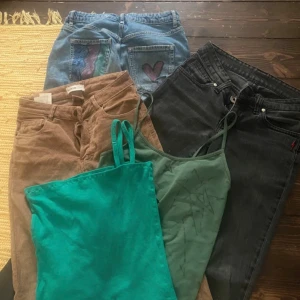 Tre par byxor i olika stilar och färger - Säljer tre par byxor: ett par ljusblå jeans med broderade bakfickor och hjärtdetalj, ett par svarta raka jeans och ett par beige manchesterbyxor med hög midja. Perfekta för dig som vill ha variation i garderoben.