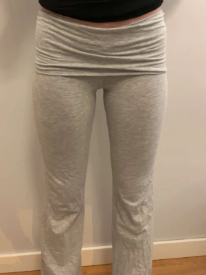 Grå mjukisbyxor med hög midja - Säljer ett par ljusgrå mjukisbyxor med bred, hög midja och raka ben. Byxorna är gjorda i mjukt bomullsmaterial och har en clean look utan synliga detaljer. Perfekta för chill dagar eller när du vill vara extra bekväm.