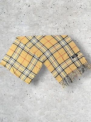 Beige Burberry halsduk - Säljer en snygg Burberry halsduk i den klassiska beige färgen med det välkända rutmönstret. Tillverkad i 100% mjuk och värmande ull.   🧵 Skick: Mycket fint skick, väl omhändertagen 🌟 Känsla: Mjuk, varm och följsam 📦 Frakt: Skickas tryggt inom 24h 📏 Mått: Längd-175, Bredd-33cm Pris kan diskuteras!