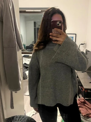 Grå stickad oversized tröja - Mysig grå stickad tröja med breda ärmar och hög krage. Tröjan har en loose och oversized passform, ribbad struktur och slitsar i sidorna. Perfekt för lager-på-lager och chill dagar.