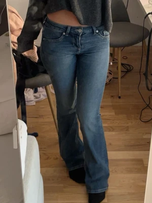 Blå bootcut jeans med låg midja - Säljer ett par klassiska blå jeans med bootcut-modell och låg midja. Jeansen har fickor, knapp- och dragkedjestängning samt en snygg tvättad finish. Perfekta för dig som gillar en retro vibe och vill ha ett par jeans som sitter tajt upptill och släpper vid benen.