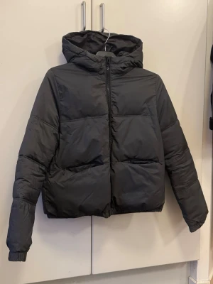 Svart pufferjacka med huva - Svart pufferjacka med skön huva och dragkedja framtill. Jackan har två stora fickor och är quiltad för extra värme. Perfekt för kalla dagar och har en loose passform som ger en chill vibe🥰