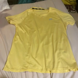 Gul t-shirt från 157 i polyester - Säljer en enkel och fräsch gul t-shirt från 157 i storlek medium. T-shirten har rund hals, korta ärmar och är gjord i ett mjukt och lätt polyestermaterial. Perfekt för dig som gillar stilrena plagg med sportig känsla.passar till träningen.