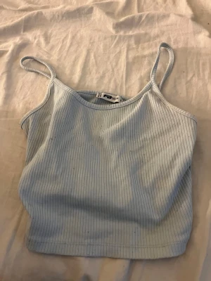Ljusblå ribbad linnetopp från new Yorker - Säljer en ljusblå ribbad linnetopp från new Yorker i storlek S. Toppen har smala axelband och är croppad i modellen. Perfekt för varma dagar och enkel att matcha med jeans eller shorts. Materialet är mjukt och stretchigt för skön passform.