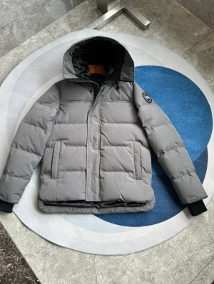 Canada Goose Macmillan grå  - ALLA STORLEKAR OCH FÄRGER! VÄSKA INGÅR! PRIS KAN DISKUTERAS Säljer en grå pufferjacka från Canada Goose med huva och svart logotyp på ärmen. Jackan har quiltad design, dragkedja och knappar framtill samt svarta muddar vid ärmsluten. Perfekt för kalla dagar och har en clean look som funkar till allt.