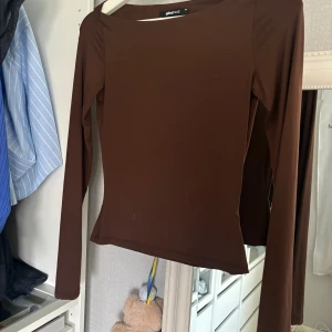 Brun långärmad topp från Gina Tricot - Snygg brun långärmad topp från Gina Tricot i storlek XS. Modellen är figurnära med rund hals och slät yta. Perfekt att styla med jeans eller kjol för en clean look. Materialet känns mjukt och stretchigt mot huden.