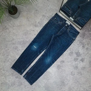 Stone Island blå jeans W32 - Snygga blå jeans från Stone Island med klassisk femficksdesign och en unik bakficka med knapp. Jeansen har en mörk tvätt med lätt slitning på låret och raka ben. Perfekta för dig som gillar streetwear och vill ha något stilrent men ändå avslappnat.